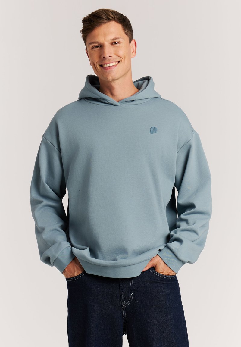 Lichtblauwe hoodie van zacht materiaal met een vo zak en een trekkoordkap, met een klein geborduurd logo op de borst.