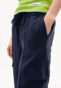 Pantalons cargo navy avec une taille élastique à cordon de serrage, dotés d'une poche latérale, fabriqués dans un tissu léger, associés à un débardeur en rib d'un vert éclatant.