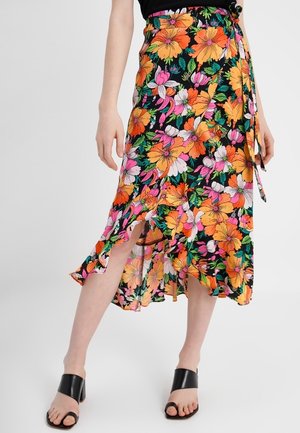 Frau trägt einen schwarzen Wickelrock mit lebhaftem orange-, rosa- und weißem Blumenmuster, kombiniert mit schwarzen offenen Sandalen mit Absatz.