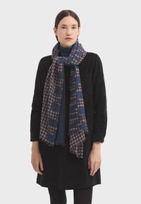 Écharpe à motifs en bleu et bordeaux, présentant un style pied-de-poule et des formes abstraites. Tissu doux avec des bords frangés, portée élégamment autour du cou.
