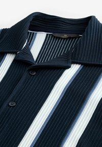Polo de canalé con rayas verticales en azul marino, azul claro y blanco. Incluye un cuello tipo polo y botones negros.