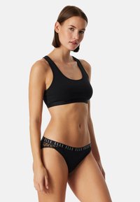 Zwarte bralette met brede bandjes en een naadloos ontwerp, gecombineerd met zwarte slips met een elastische tailleband met merklogo en kanten accenten.