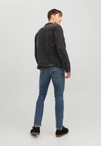 Veste en denim noir au design classique, associée à un jean slim bleu. La veste présente des poignets boutonnés et un détail de empiècement au dos.