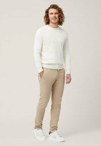 Maglione lungo a maniche, pantaloni chinos beige chiaro e sneakers bianche con dettagli neri. Tessuto morbido, design aderente e dettagli minimi.