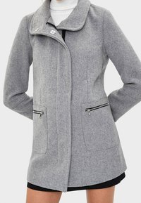 Gråullskappa med krage, dragkedjsfickor och rak passform. Har en slät yta och moderna designelement.