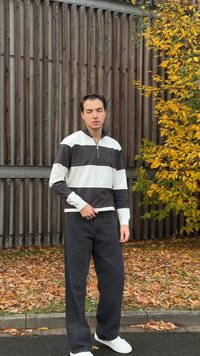 Negyedig zipzáras pulóver fekete-fehér vízszintes csíkokkal, könnyű anyagból, hosszú ujjakkal. Laza fekete nadrággal és fehér sportcipővel párosítva.