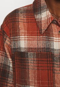 Rood-zwart geruit flanellen overhemd met een kraag, knopen en een gestructureerde stof met contrasterende witte lijnen in het patroon.