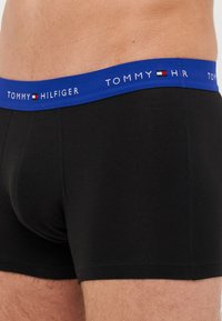 Fekete pamut boxer alsónadrág széles kék gumival, amelyen a "TOMMY HILFIGER" logó fehér színben látható. Simaság, testhez simuló kivitel.