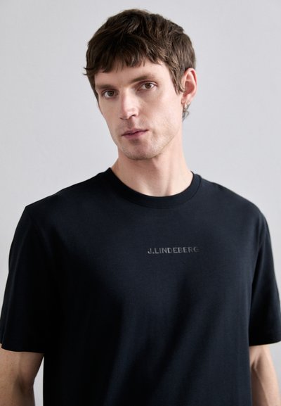 Camiseta de algodón negra con manga corta y cuello redondo, que presenta un logo "J.LINDEBERG" sutilmente grabado en la parte frontal.