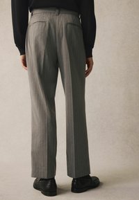 Un pantalon gris à rayures, avec une coupe droite, présentant deux poches arrières et des chaussures noires, vu de dos.