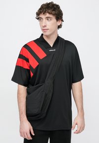 Čierny športový dres s červenými horizontálnymi pruhmi, ľahkým materiálom, krátkymi rukávmi a výstrihom do v, doplnený čiernou crossbody taškou.