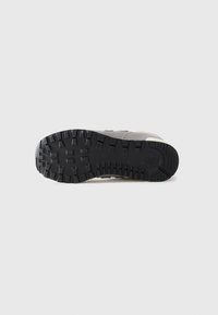 Semelle de sneaker grise avec un motif de semelle noir profond, montrant un design de grip et un logo près du talon sur un fond gris clair.