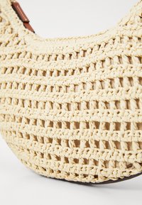 Pletená béžová taška s otevřenou pleteninou, texturovaným materiálem, zakřiveným tvarem a hnědými koženými detaily.