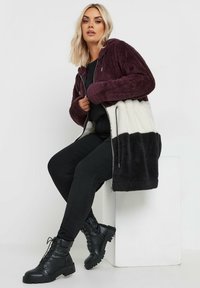 Chaqueta de forro polar con capucha, que presenta un diseño en bloques de colores: morado oscuro, blanco y negro. Tejido texturizado, cierre con cremallera, bolsillos laterales.