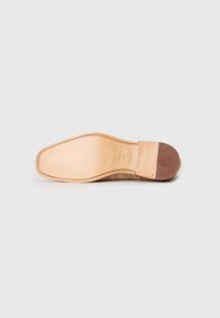 Suela de zapato de cuero con una superficie lisa beige, un tacón de goma marrón y costuras visibles a lo largo del borde, junto con detalles de marca.