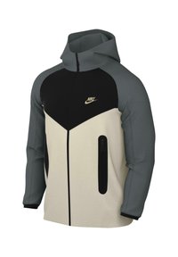 Giacca con cappuccio dal design a blocchi di colore in crema, nero e grigio. Presenta una chiusura frontale con zip, due tasche laterali e un dettaglio logo in oro.