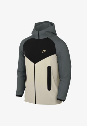 Giacca con cappuccio dal design a blocchi di colore in crema, nero e grigio. Presenta una chiusura frontale con zip, due tasche laterali e un dettaglio logo in oro.
