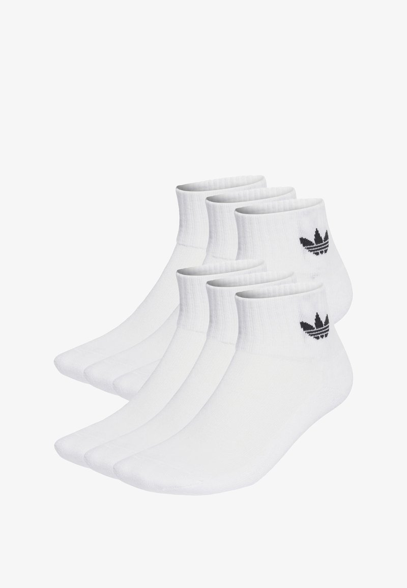 Bele nogavice iz bombaža do gležnjev z rebrastimi manšetami in črnim logotipom Adidas. Pet parov je urejenih v vrsto, kar prikazuje gladko teksturo in enotno obliko.