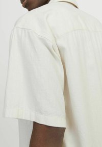 Lichtbeige linnen overhemd met korte mouwen, voorzien van een klassieke kraag en een losse pasvorm, met een gladde textuur en minimale stikseldetails.