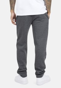 Grijze sweatpants van zacht materiaal, met een elastische tailleband, zijzakken en een relaxte pasvorm, gecombineerd met witte sneakers.