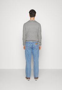 Un pull en tricot gris avec un col rond, associé à un jean en denim bleu clair. Les jeans présentent des poches arrière et une patch en cuir brun.