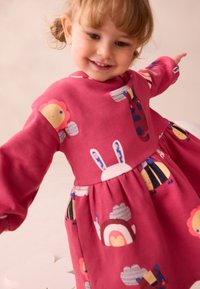 Lyserød bomuldsbuket med en rynket nederdel, lange ærmer og legesyge dyre- og forme mønstre i klare farver.