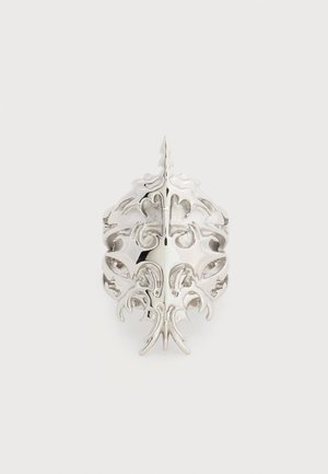 Bague en argent ornée d'un design symétrique et délicat de filigrane, évoquant des feuilles et des motifs floraux sur un fond uni.