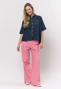 Denim overhemd met korte mouwen en knoopsluiting, gecombineerd met roze gestreepte broek met wijde pijpen. Voorzien van een klein logo op het overhemd en een comfortabele, losse pasvorm.