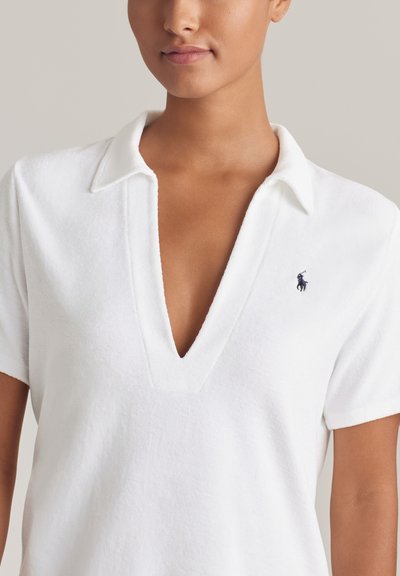 Λευκό πόλο μπλουζάκι από απαλό ύφασμα, με βαθύ V-λαιμόκοψη, κοντά μανίκια και μικρό ναυτικό λογότυπο στο στήθος.