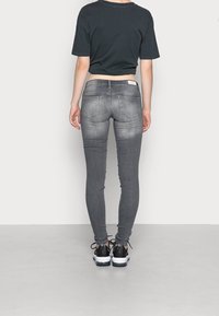 Jeans ajustados grises con detalles de desgaste, dos bolsillos traseros y una cintura alta, combinados con una camiseta negra básica de corte cropped y zapatillas negras.