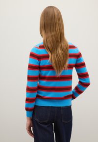 Maglione a righe con strisce orizzontali blu e rosse, texture lavorata a maglia, polsini e orlo a coste, abbinato a jeans blu scuro.