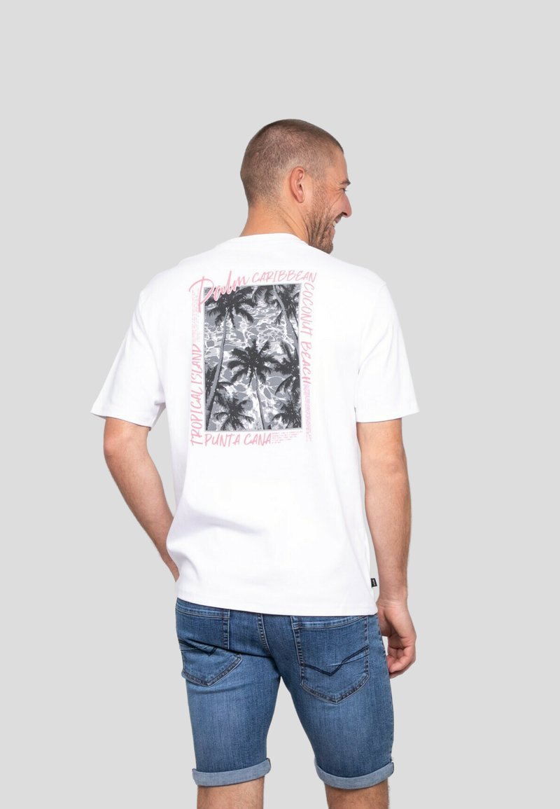 T-shirt blanc avec un graphique de palmier noir et blanc et un texte rose indiquant "Punta Cana, Île Tropicale, Plage de Coco" au dos.