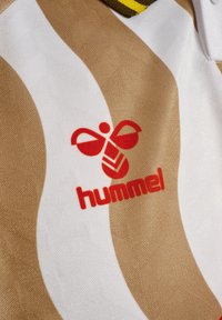 Vit och beige randig tyg med en texturerad yta. Har en röd "hummel"-logotyp med en stiliserad bi-design nära det övre vänstra hörnet.
