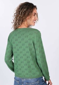 Grüner Langarmpullover mit einem leichten Texturmuster. Rundhalsauschnitt und gerippte Bündchen, kombiniert mit Denim-Jeans.