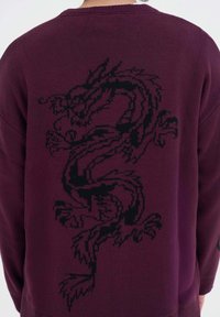 Burgundská pletená svetr s texturovaným černým designem draka, který je výrazně zobrazen na zadní straně, klasickým kulatým výstřihem a pohodlným střihem.