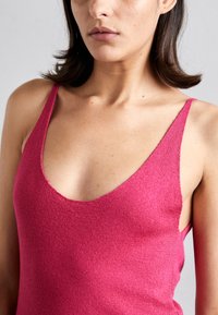 Top aderente senza maniche di colore rosa, con scollatura a V profonda, realizzato in un morbido tessuto a maglia testurizzato. Cuciture visibili lungo i bordi.