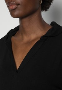 Černá mikina s výstřihem do V, vyrobená z měkké, strukturované látky. Má volný střih a malou přední kapsu.