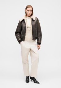 Καφέ δερμάτινο μπουφάν bomber με γούνινο γιακά σε κρεμ χρώμα, συνδυασμένο με μπεζ πουλόβερ και κρεμ παντελόνι. Ολοκληρώνει την εμφάνιση με μαύρες μπότες με τακούνι.