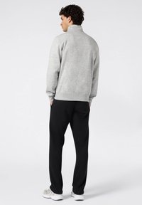 Sudadera de forro polar gris con cuello alto, puños y dobladillo acanalados, combinada con pantalones deportivos negros. El modelo se ve desde la parte de atrás.