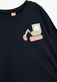 Marineblå bomulds T-shirt med et beige og pink broderet gravemaskine-design på venstre brystområde. Korte ærmer, rund halsudskæring.