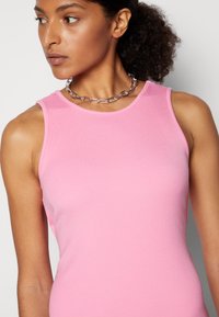 Top de malha rosa ajustado com decote redondo. Apresenta design sem mangas e uma textura subtil. Acentuado com um colar de corrente prateada.