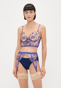 Set de lenjerie cu un bralet din dantelă florală, de culoare albastru închis, curea de suspensor asortată și ciorapi din dantelă nude, cu bretele ajustabile.