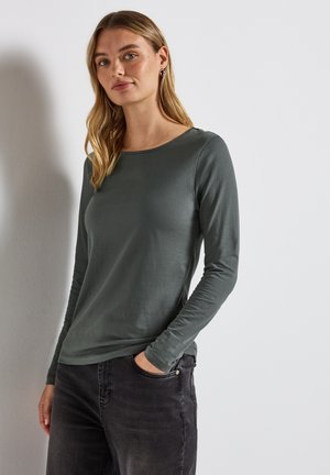Mørkegrøn langærmet skjorte i blødt stof med rund halsudskæring, tætsiddende design og glat tekstur, parret med mørke jeans.