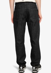 Černé džíny z denimu s volnějším střihem, vybavené dvěma zadními kapsami a jemnými šicími detaily. Kombinovány s černými teniskami.