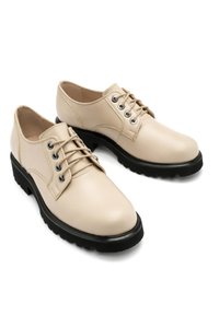 Beige lædersko med en glat finish, rund tå, sort gummisål og seks snøringer.