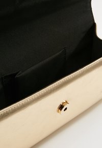 Petit porte-monnaie doré avec intérieur en tissu noir, ouvert pour montrer la poche intérieure et la fermeture magnétique sur le rabat avant.