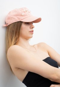 Rosa Stoffkappe mit weißen Perlenakzenten, gebogenem Schirm und verstellbarem Riemen hinten. Getragen von einem Modell mit langen Haaren.