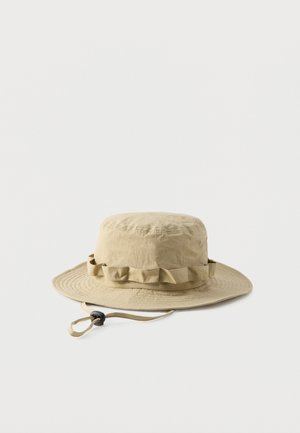 Beige wide-brim outdoor hat with chin strap and adjustable toggle, featuring a gathered fabric band around the crown.