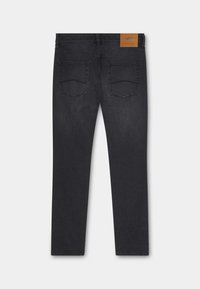 Jeans de mezclilla oscura, corte ajustado, con una parche de cuero marrón claro en la cintura y dos bolsillos traseros con costuras curvas. Textura suave, desgaste mínimo.