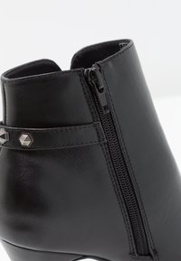 Černá kotníková bota s hladkým koženým povrchem, bočním zapínáním na zip a ozdobným páskem s hexagonálními cvočky.